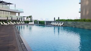 A modern pool area with lounge chairs and umbrellas, surrounded by buildings with glass railings and a clear view of the city skyline. - PVH - Stunning 2BR - Creek Vistas Grande (Dubai)