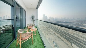 A balcony with a view of a city skyline, two wicker chairs, a small table, and a potted plant. - PVH - Stunning 2BR - Creek Vistas Grande (Dubai)