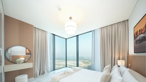 A modern hotel room with a large bed, a vanity with a mirror, and a view of the cityscape through floor-to-ceiling windows. - PVH - Stunning 2BR - Creek Vistas Grande (Dubai)