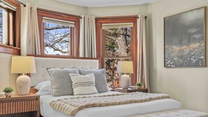 A bedroom with a large bed, two bedside tables, a bench, and a window with curtains. - Walk Downtown + Hot Tub + Sauna + Game Room + Pets (Wisconsin Dells)