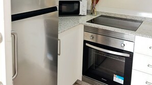 Een functionele keuken met een roestvrijstalen koelkast, een magnetron, een inbouwoven en witte kastjes.