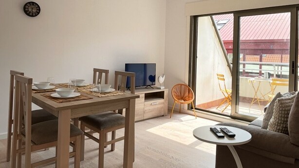 Een moderne woonkamer met een eethoek, een bank, een televisie en een balkon met gele stoelen.