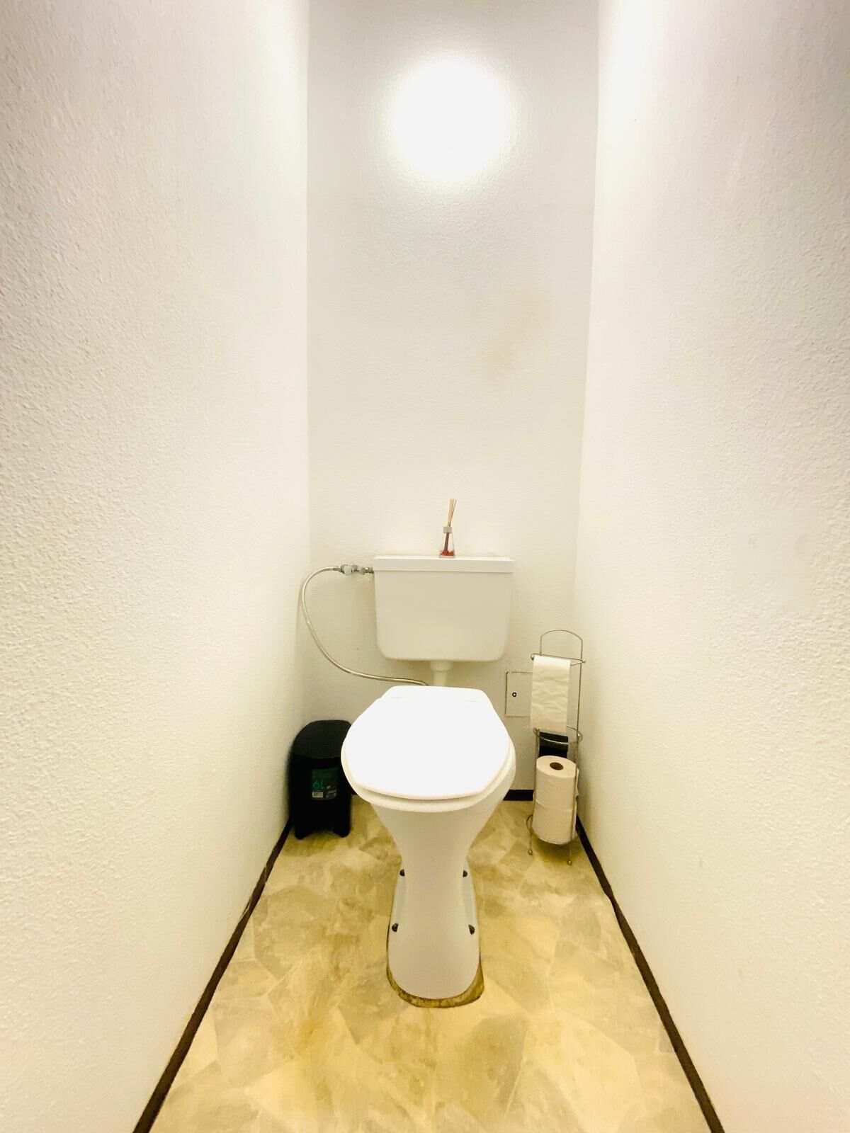 A narrow bathroom with a white toilet, a black trash bin, and a toilet paper holder.