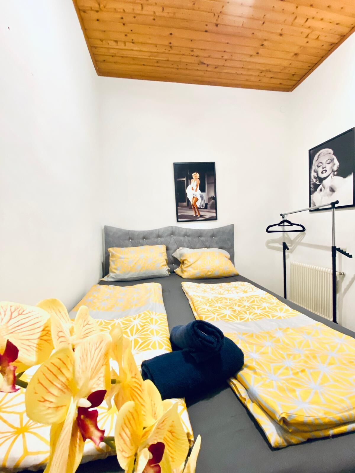 A bedroom with two beds, a grey upholstered headboard, and a radiator.