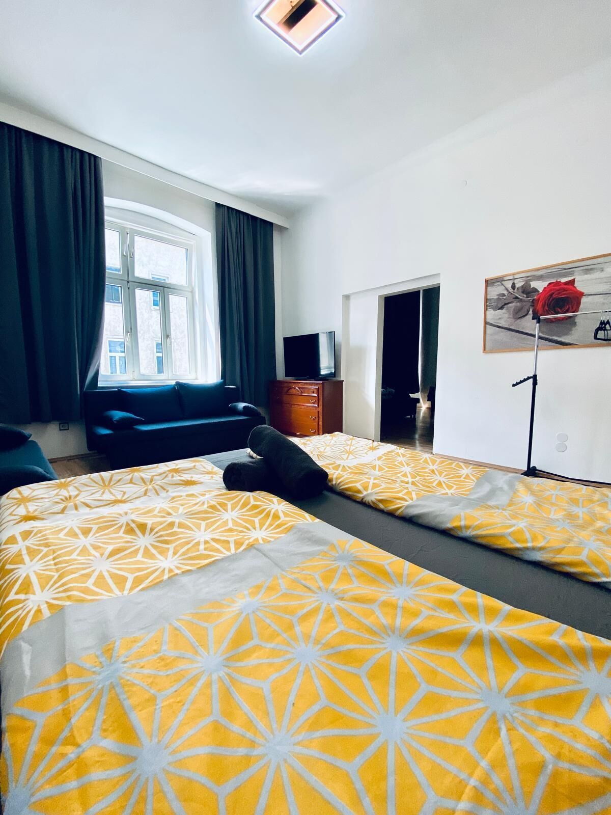 Et hotelværelse med to senge, et fjernsyn, en kommode og et vindue med gardiner.