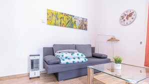 A modern living room with a grey sofa, a glass coffee table, a radiator, a world map clock, and a colorful abstract painting. - Spacious 5BR Apt Close to Augarten (Vienna)
