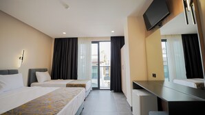 Habitación de hotel con dos camas, un escritorio, un televisor y una puerta corrediza de vidrio al exterior.