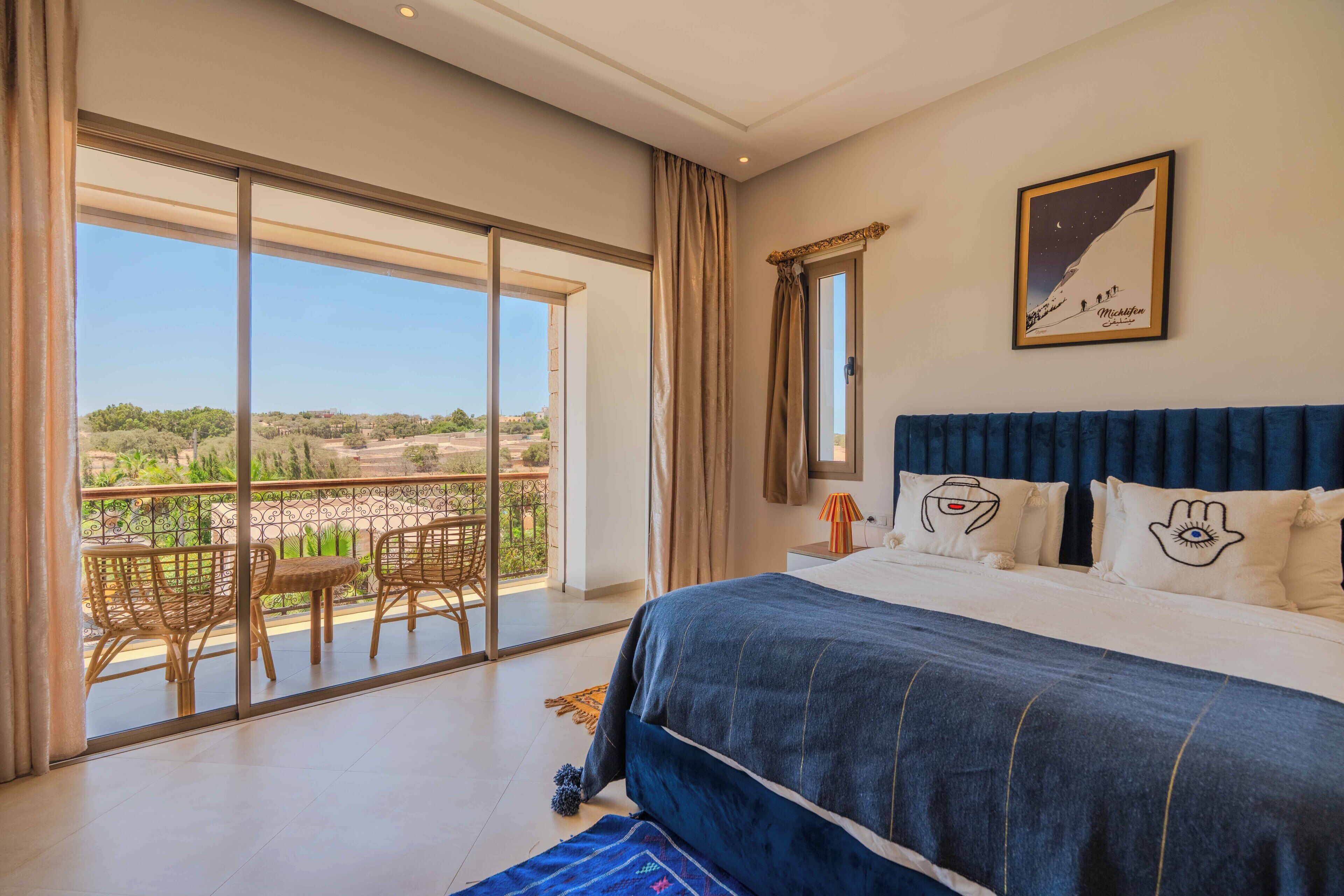 Een slaapkamer met een groot bed, een balkon met rieten meubels en een ingelijst schilderij aan de muur.
