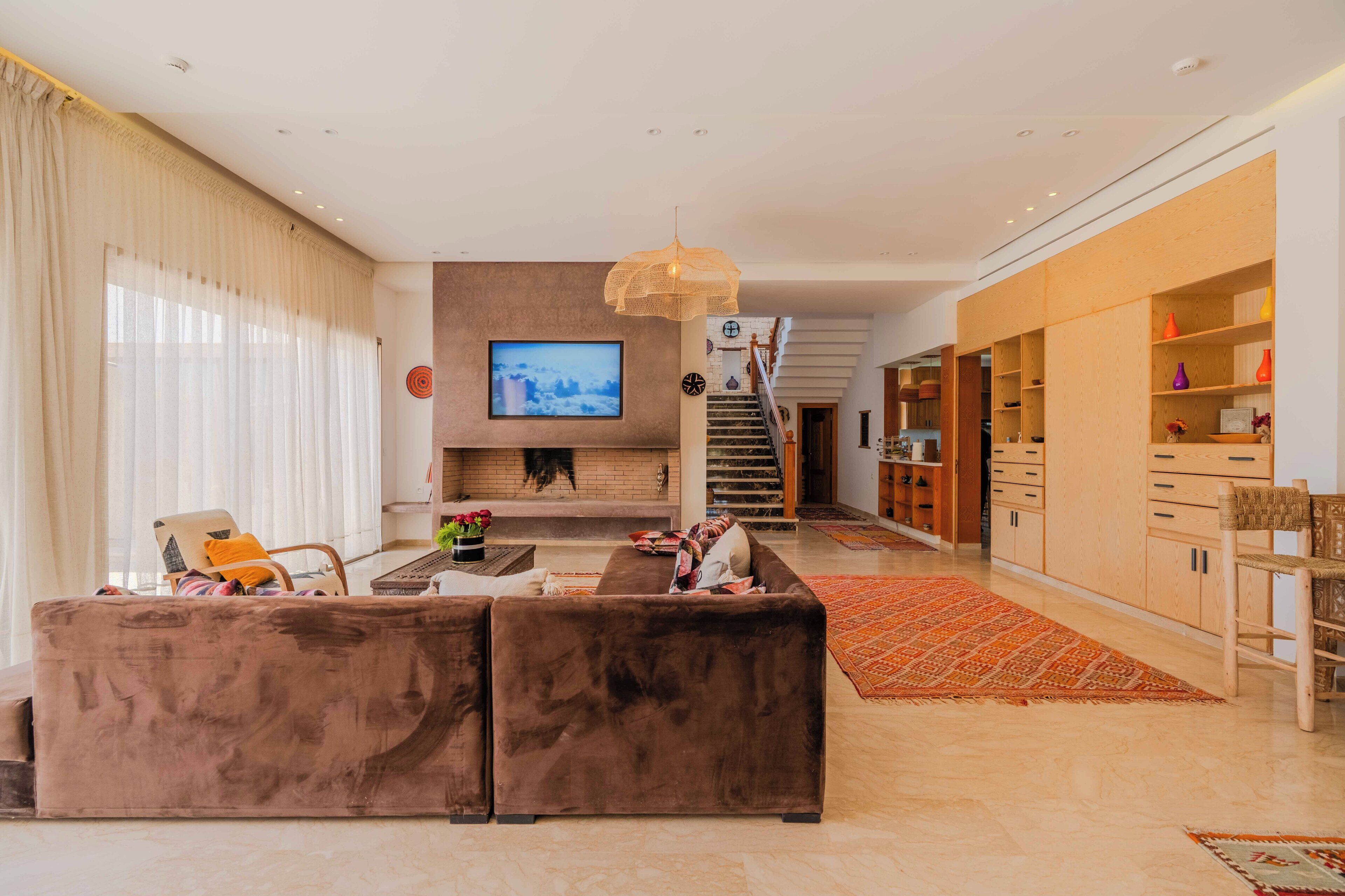 A modern living room with a large flat-screen TV, a fireplace, a sofa, and a staircase leading to another level.