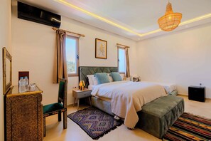 A bedroom with a bed, bedside tables, a chair, a rug, and a hanging light fixture.