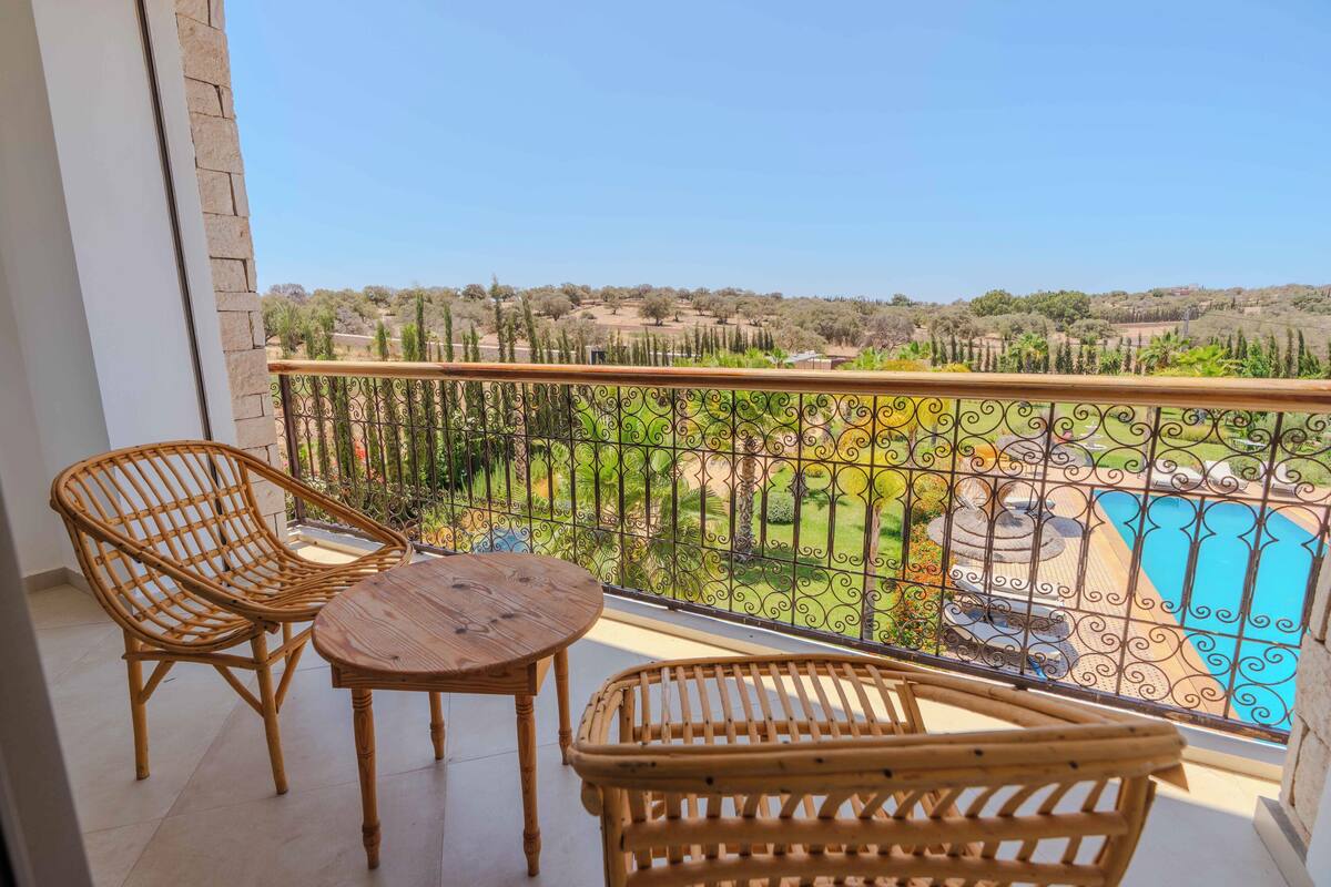 A balcony with wicker furniture and a view of a pool and greenery.