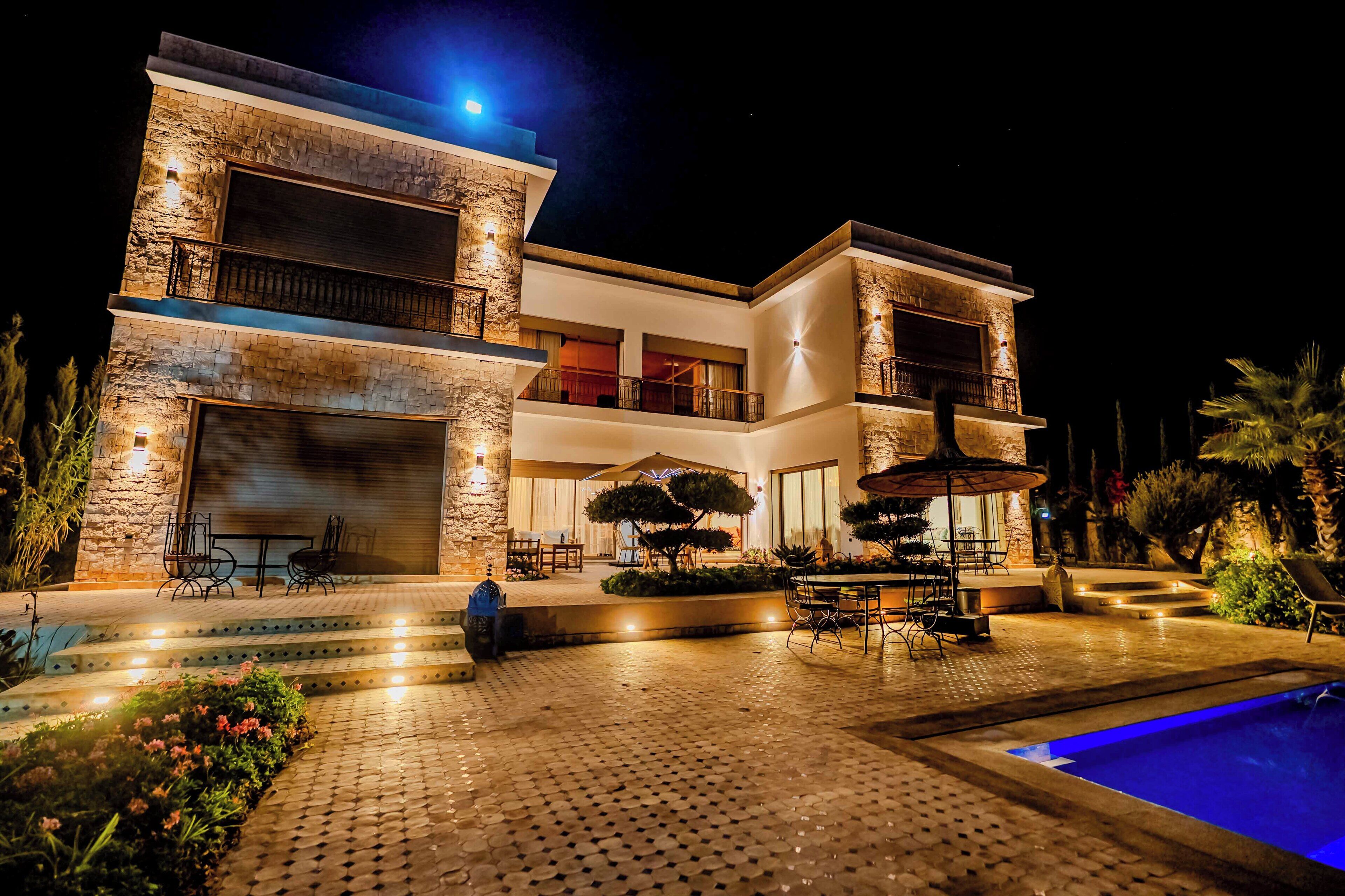 A modern two-story house with a swimming pool, outdoor seating, and a well-lit patio area.