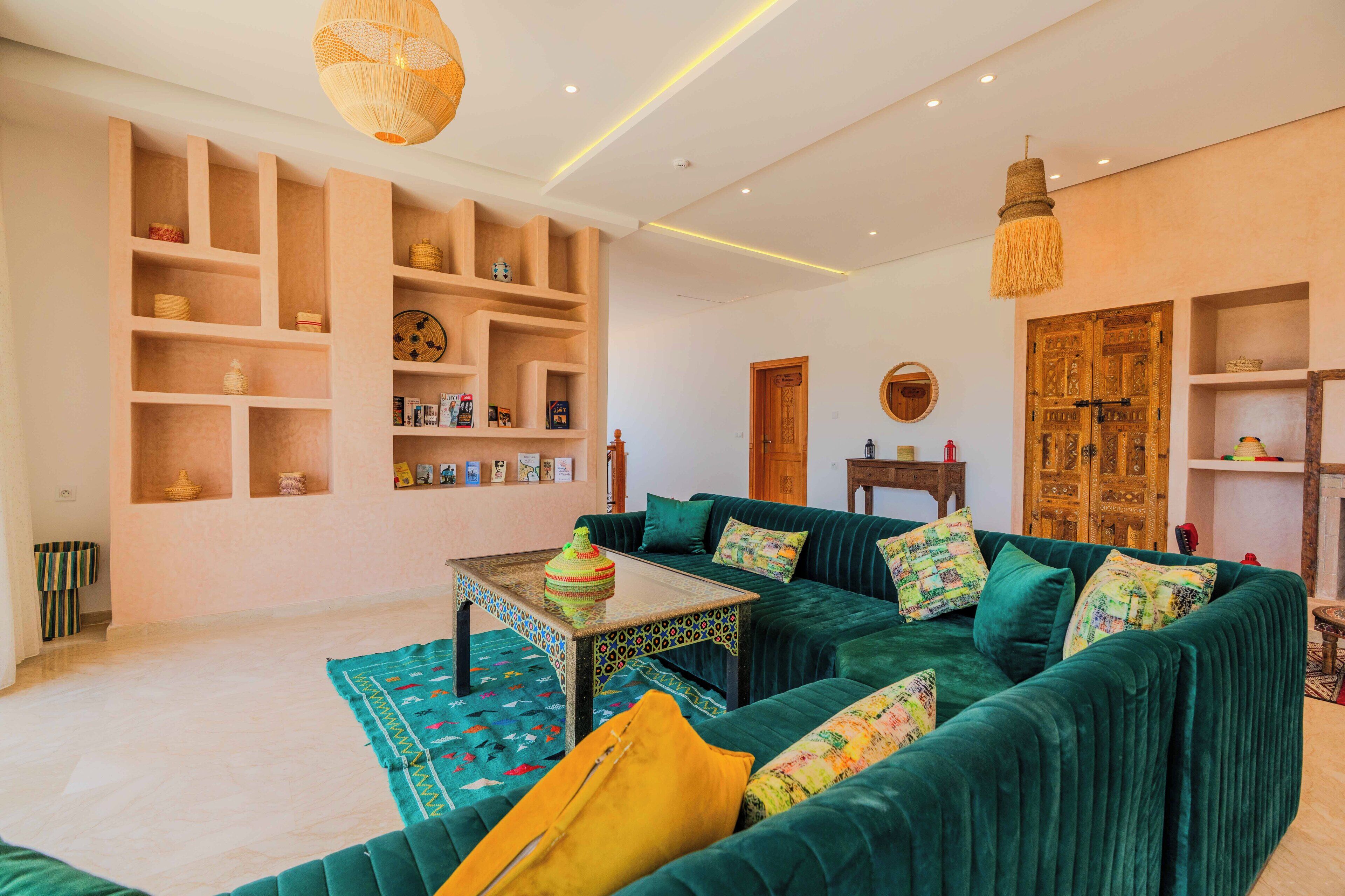 Una sala de estar con un sofá verde, una mesa de centro estampada y estanterías de madera con adornos.