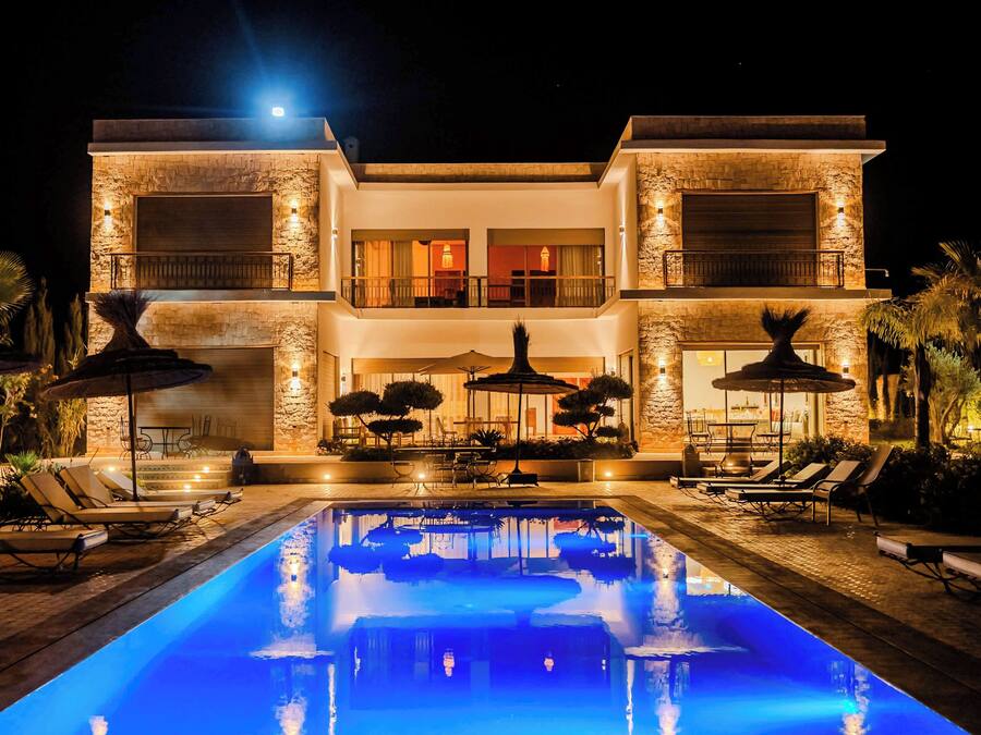 A two-story modern house with a swimming pool, outdoor furniture, and a well-lit patio area.