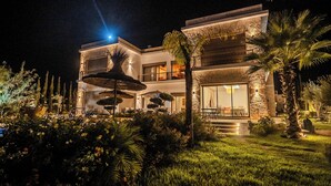Una casa moderna de dos plantas con una entrada bien iluminada, una zona de estar exterior cubierta y un jardín exuberante.