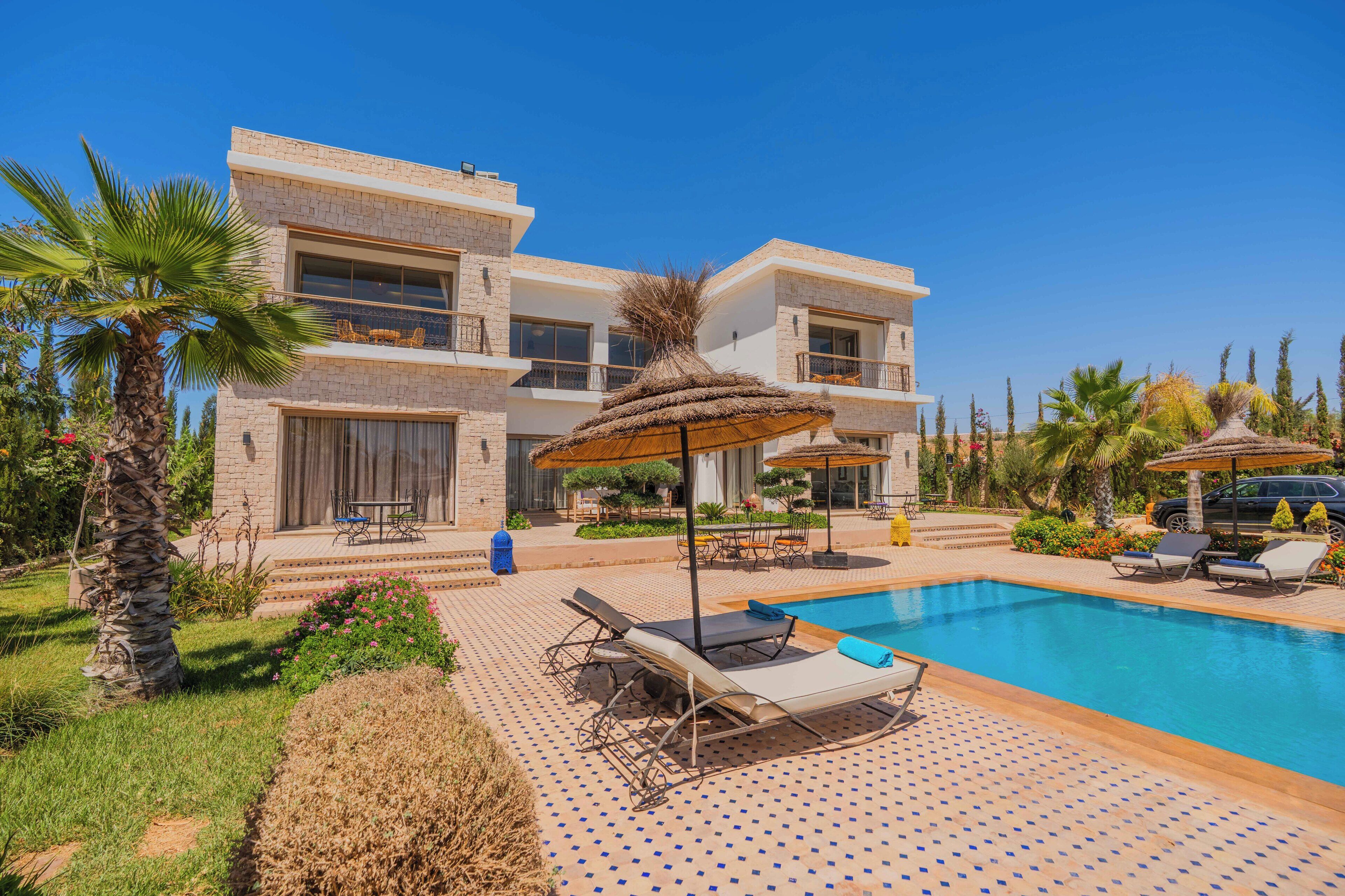 A modern two-story hotel with a swimming pool, lounge chairs, and a patio area.