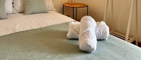 A hotel room with a bed, pillows, a bedside table with a lamp, and a towel rack.