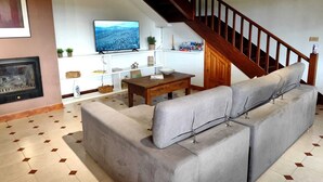 A living room with a grey sofa, wooden staircase, and a flat-screen TV on the wall. - Airtegal Casa do Pepe (Cedeira)