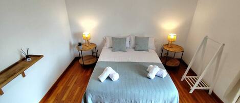 A neatly arranged bedroom with a bed, two bedside tables with lamps, a wooden shelf, and a white radiator.