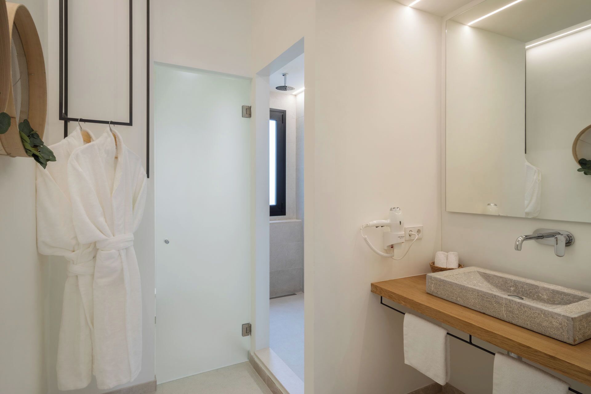 Un baño moderno con tocador de madera, un espejo grande y una zona de ducha visible a través de una puerta abierta.
