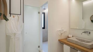 Un baño moderno con tocador de madera, un espejo grande y una zona de ducha visible a través de una puerta abierta.