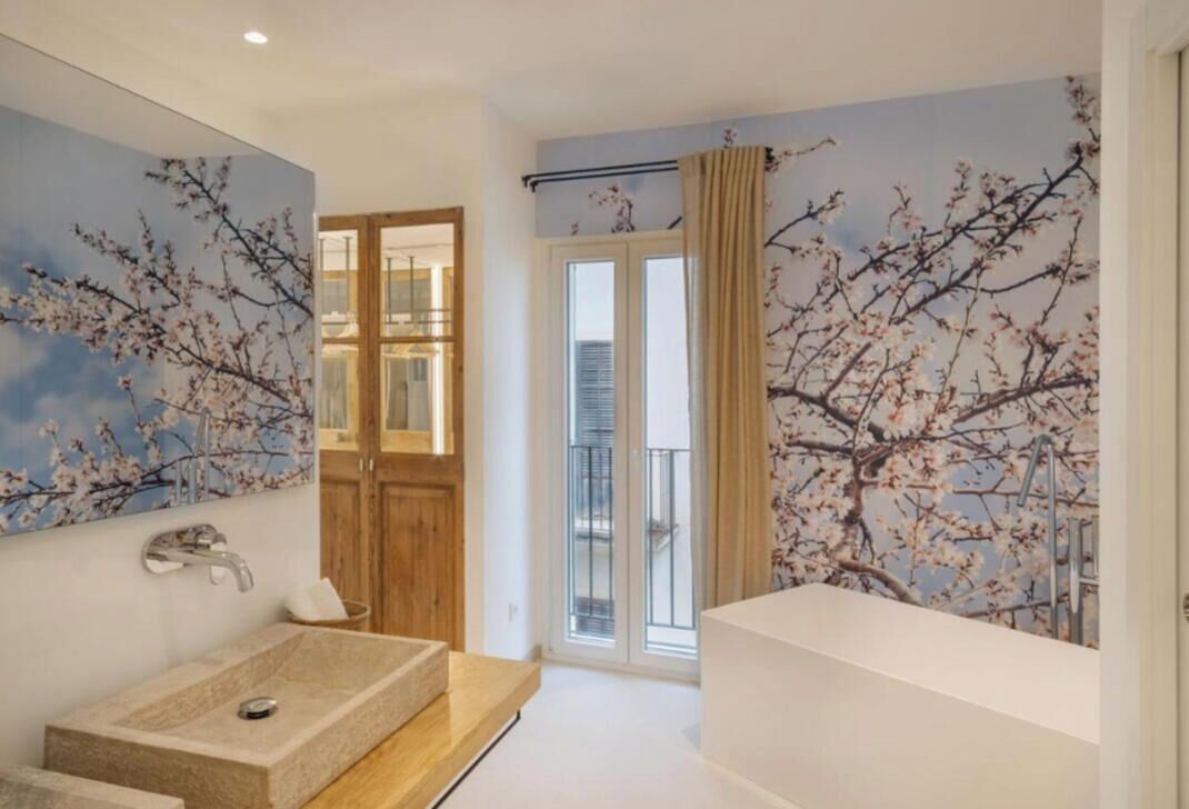 Un bagno moderno con un lavandino grande, una vasca da bagno e una doccia. Una porta conduce a un balcone con vista sulla città.