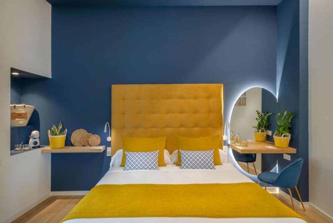 Ein Schlafzimmer mit einer gesteppten Kopfteile, einem Nachttisch mit Spiegel, einem Sessel und einem kleinen Schreibtisch mit Lampe.