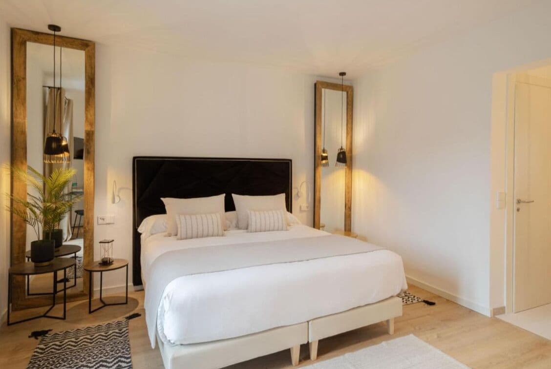 Een moderne slaapkamer met een groot bed, een nachtkastje, een spiegel en een potplant.