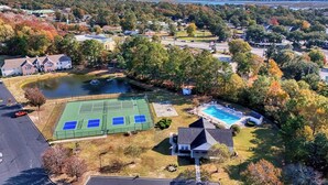 Ett flygbildsfoto av ett bostadsområde med en tennisbana, en swimmingpool och hus omgivna av träd.