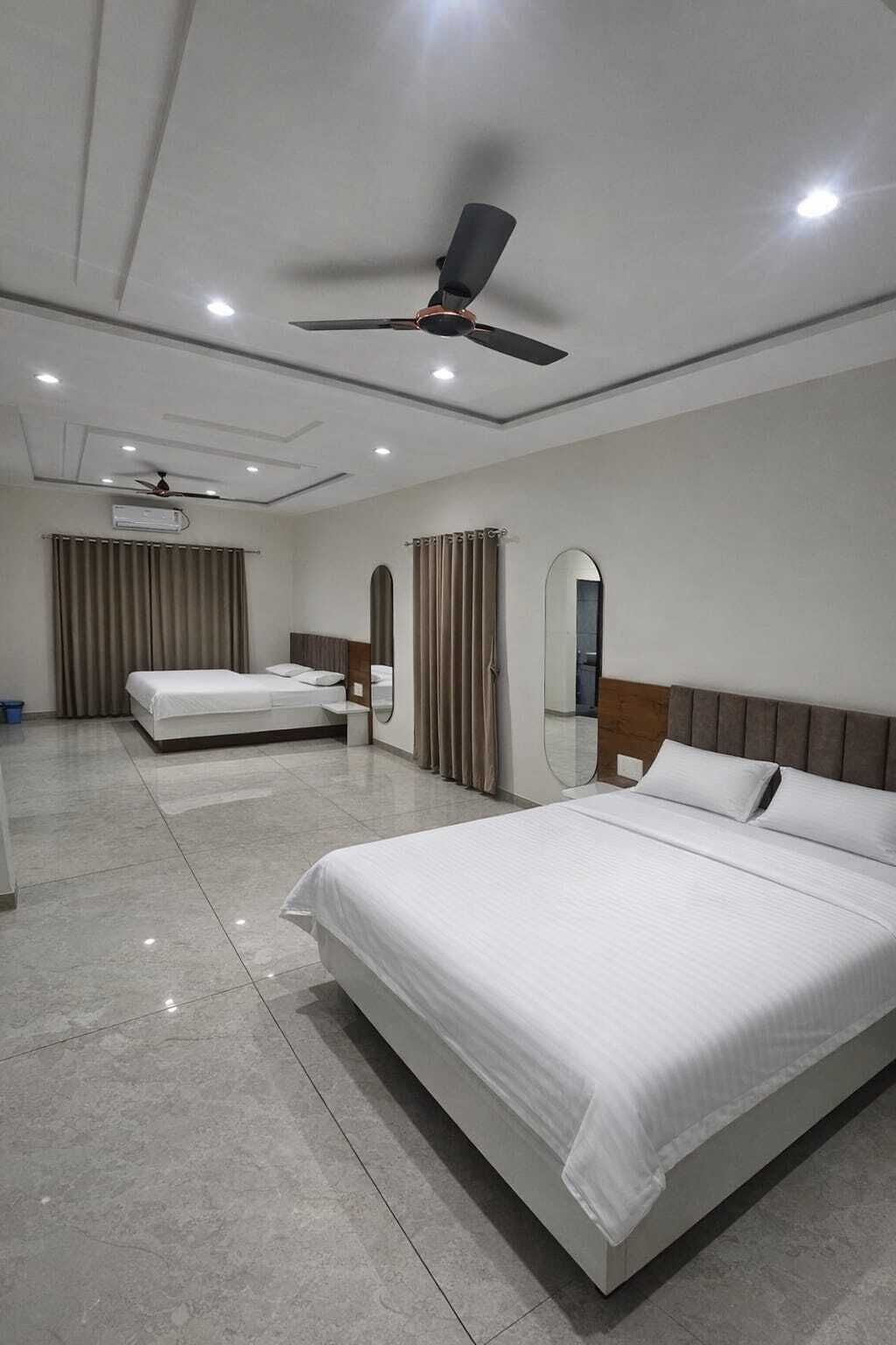 A hotel room with a large bed, a smaller bed, a ceiling fan, and a mirror.