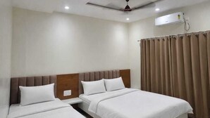 Habitación de hotel con dos camas, ventilador de techo, iluminación empotrada y una ventana con cortinas.