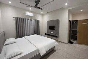 A modern hotel room with a bed, a television mounted on the wall, a ceiling fan, and a door leading to a closet. - Hotel Abhishek Pride  (Shani Shingnapur)