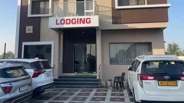Hotel llamado 'Hotel Abhishek Pride' con un cartel de 'Lodging'. Hay dos coches aparcados delante.