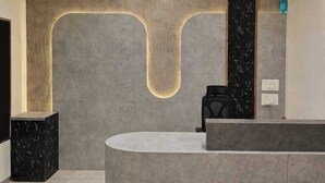 Zona de recepción con mostrador curvo, ventilador de techo, iluminación empotrada y suelo de mármol.