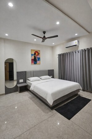 A modern bedroom with a bed, ceiling fan, air conditioning unit, and a painting on the wall. - Hotel Abhishek Pride (Shani Shingnapur)