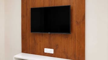 A flat-screen TV mounted on a wooden wall with a white shelf below.