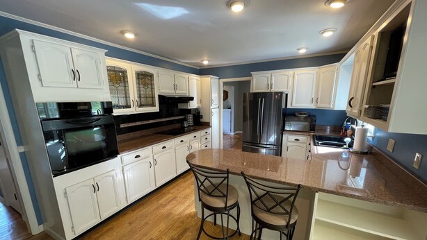 A modern kitchen with white cabinets, stainless steel appliances, and a wooden floor.