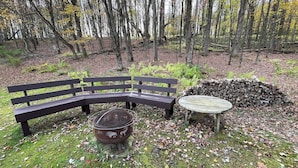 A bench and a table in a forested area with a pile of logs.