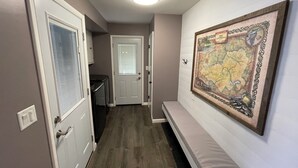 A hallway with a wooden floor, a door with a window, a wall-mounted map, and a ceiling light.