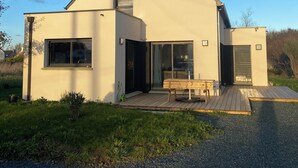 A modern two-story house with a large deck, a sliding glass door, and a small outdoor table. - A comfortable home in Kérity, just a stone's throw from the sea (Penmarch)