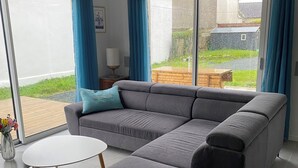 A modern living room with a grey sectional sofa, a small white table, and a glass coffee table. - A comfortable home in Kérity, just a stone's throw from the sea (Penmarch)