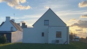 A white building with a triangular roof, a small window, and an air conditioning unit on the side. - A comfortable home in Kérity, just a stone's throw from the sea (Penmarch)