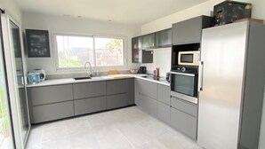 A modern kitchen with grey cabinets, a stainless steel refrigerator, a microwave, and a sink. - A comfortable home in Kérity, just a stone's throw from the sea (Penmarch)
