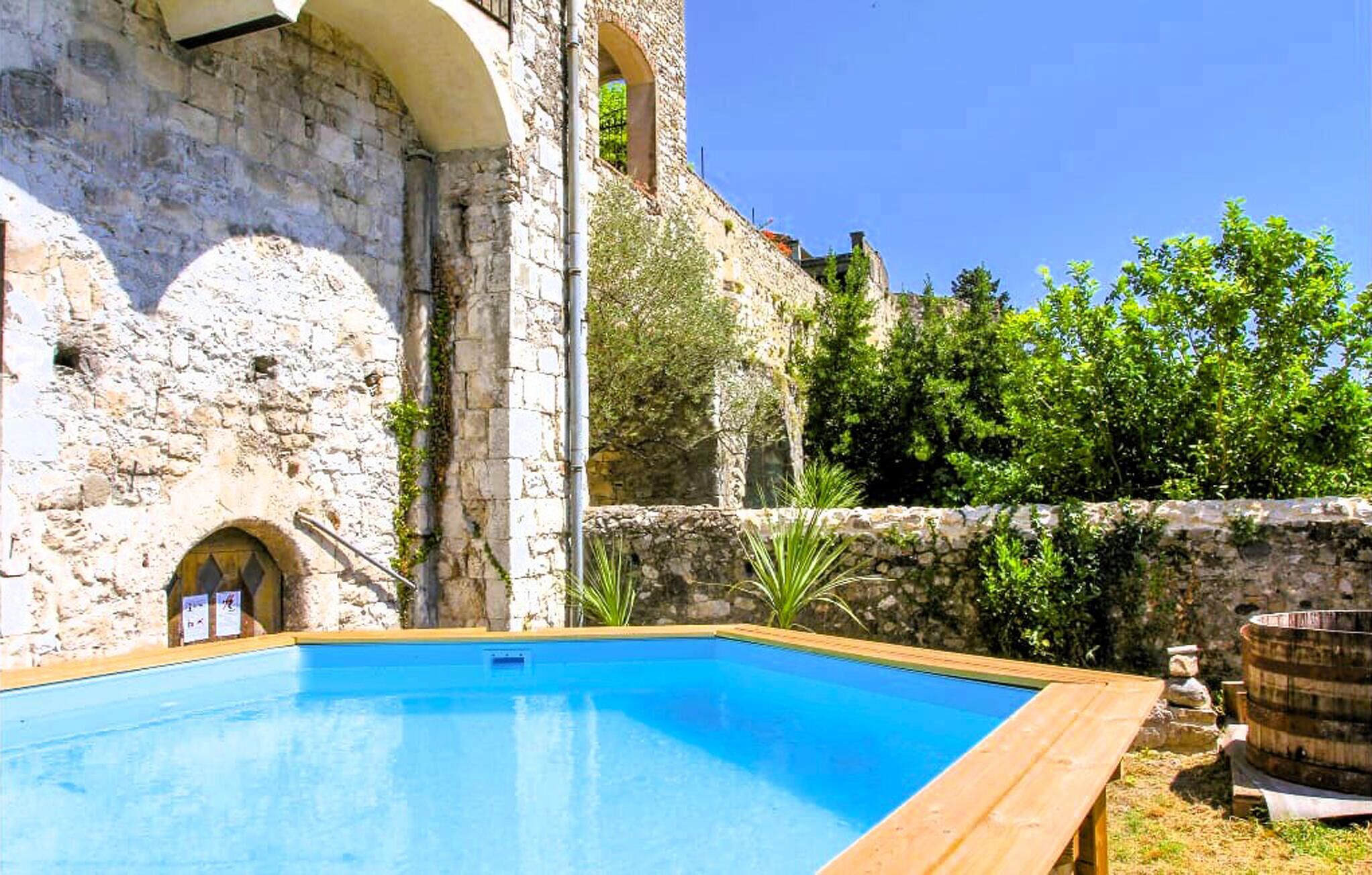Una piscina junto a un edificio de piedra con ventanas de arco y una torre.