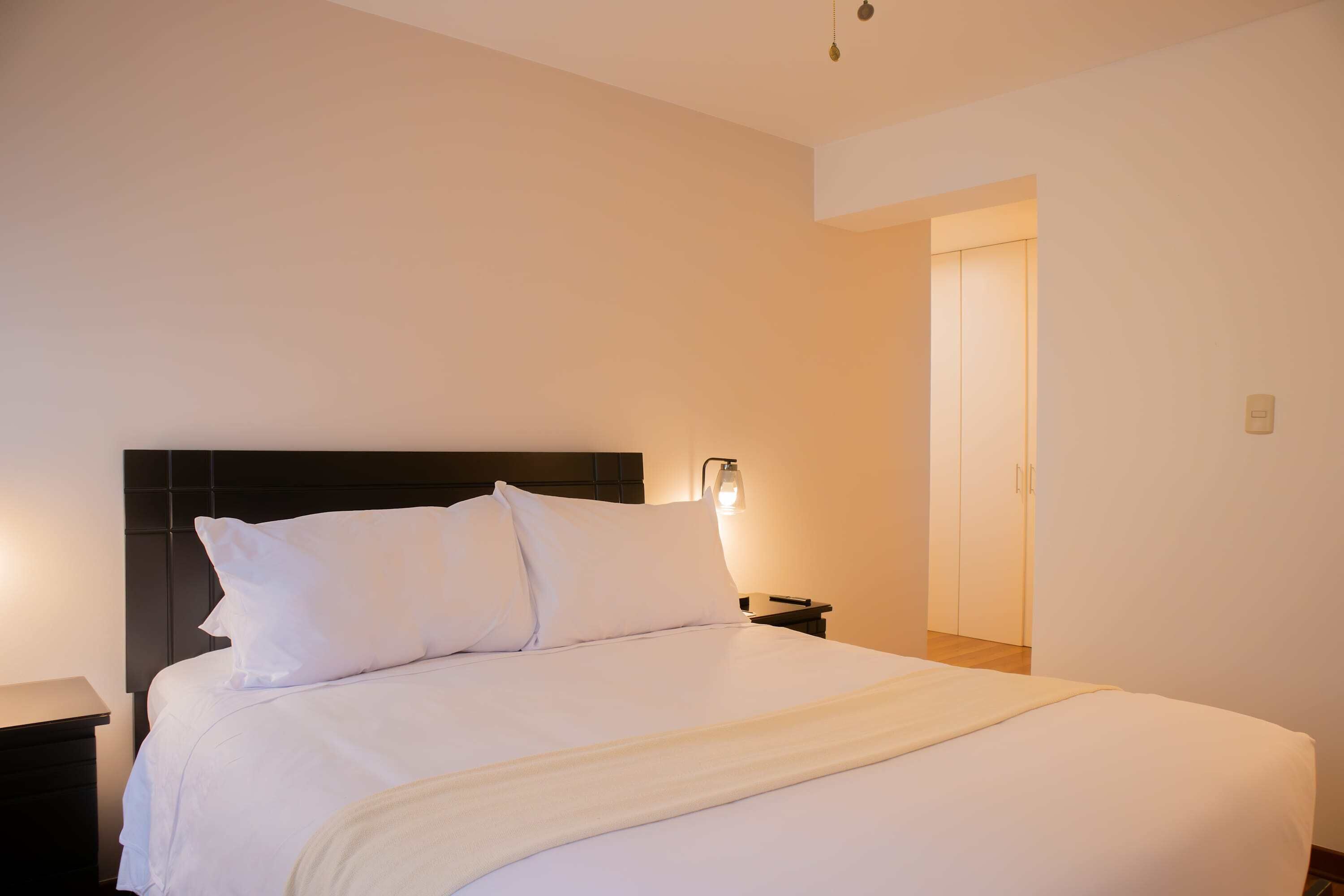 A neatly made bed with white linens and a dark headboard in a hotel room.
