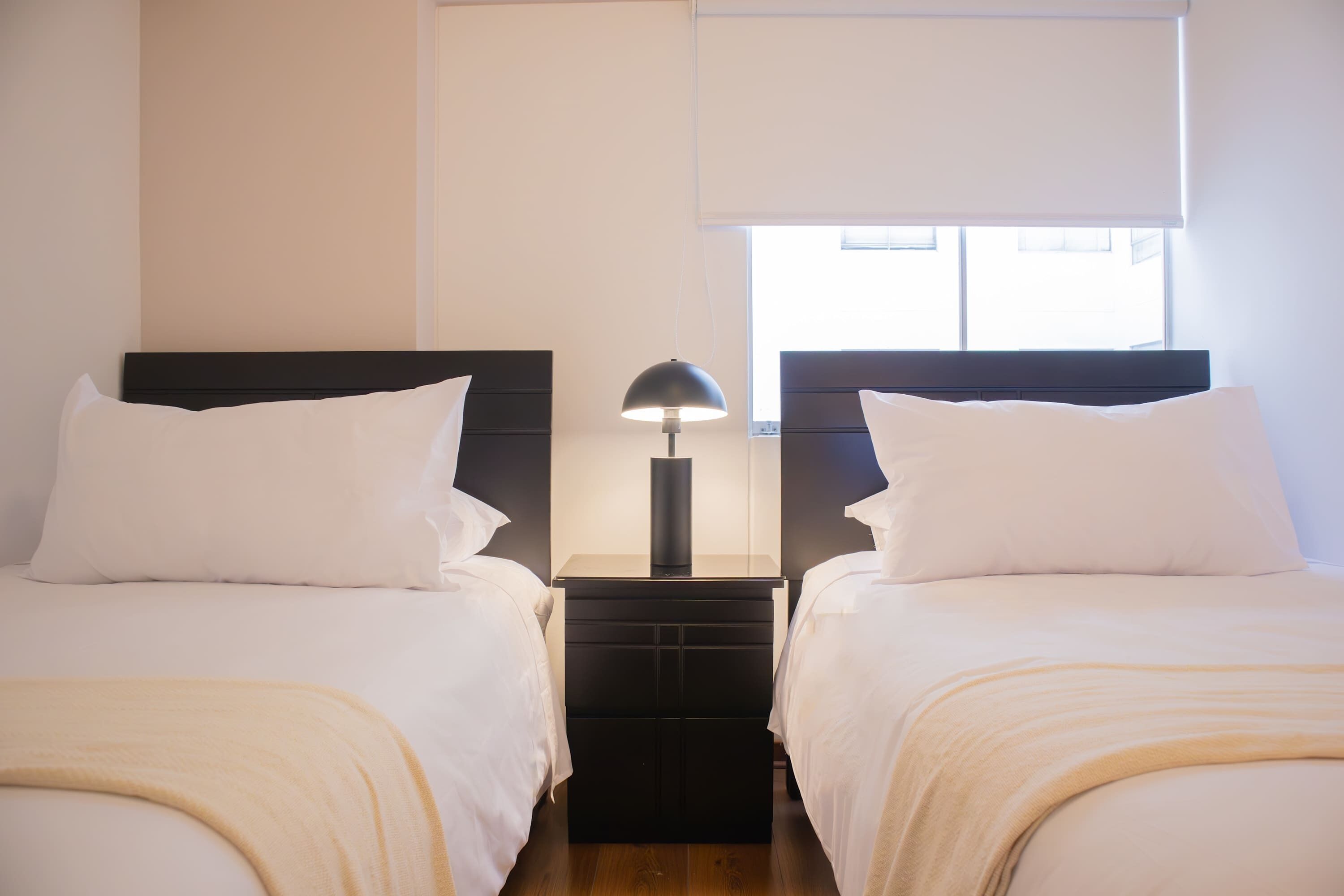 Una camera d'albergo con due letti, un comodino con una lampada e una finestra con persiane.