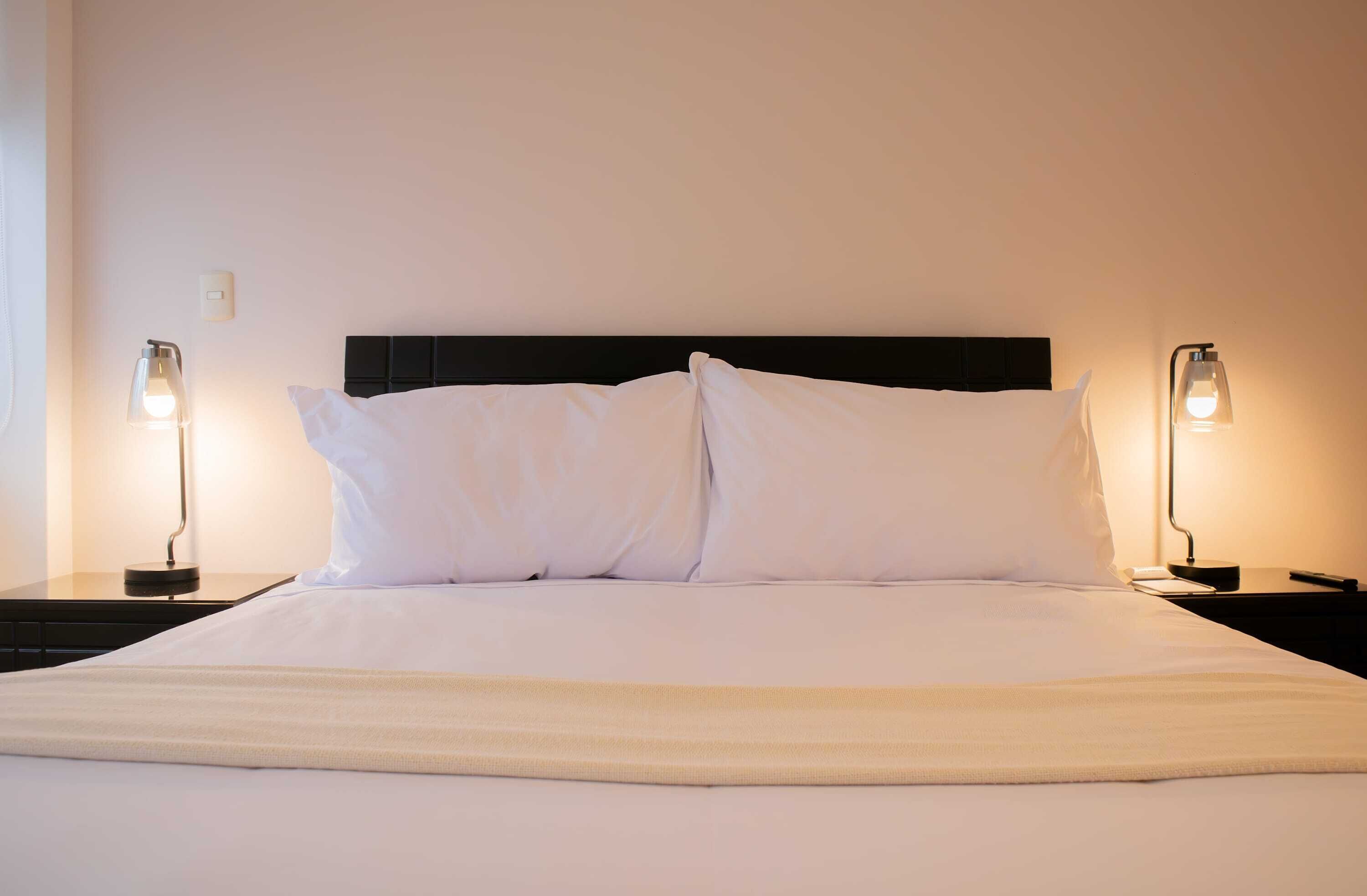 A neatly made bed with white linens, two bedside lamps, and a black headboard.