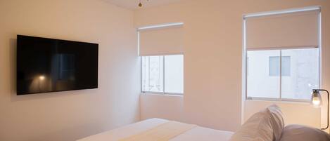 Ein Schlafzimmer mit einem Bett, Deckenventilator, einem Wand-Fernseher und zwei Fenstern mit Jalousien.