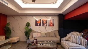 Un salon moderne avec un canapé, un fauteuil et une table basse. Trois œuvres d’art encadrées ornent le mur, et un ventilateur de plafond est installé au plafond.