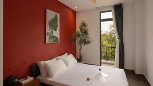 Une chambre d’hôtel comprenant un lit, une table de chevet, un ventilateur de plafond, une fenêtre avec des rideaux et un balcon agrémenté d’une plante.